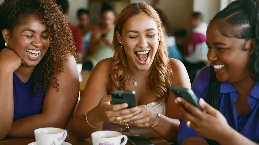 Amigas num café rindo de um vídeo no celular